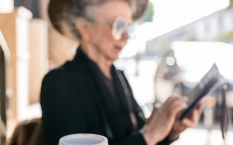 Image shows an elderly woman sitting with a disposable cup of coffee, which has been shown to release microplastics