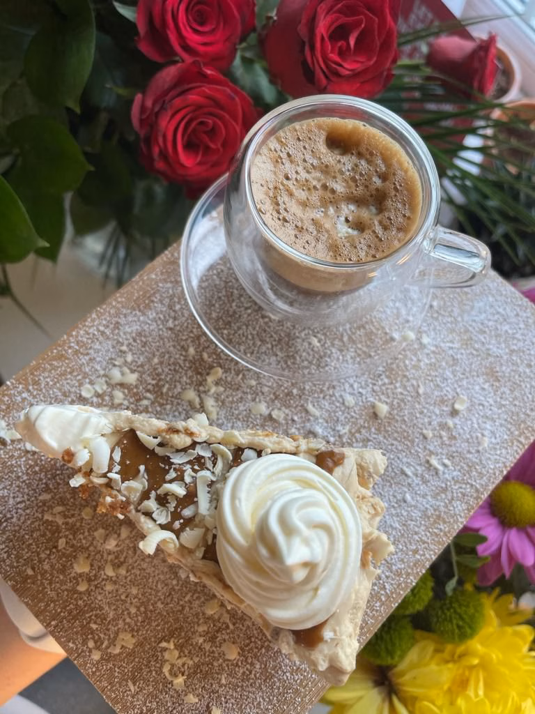 Foto di una fetta di biscoff vegan cheesecake fatta in casa accanto a un caffè.